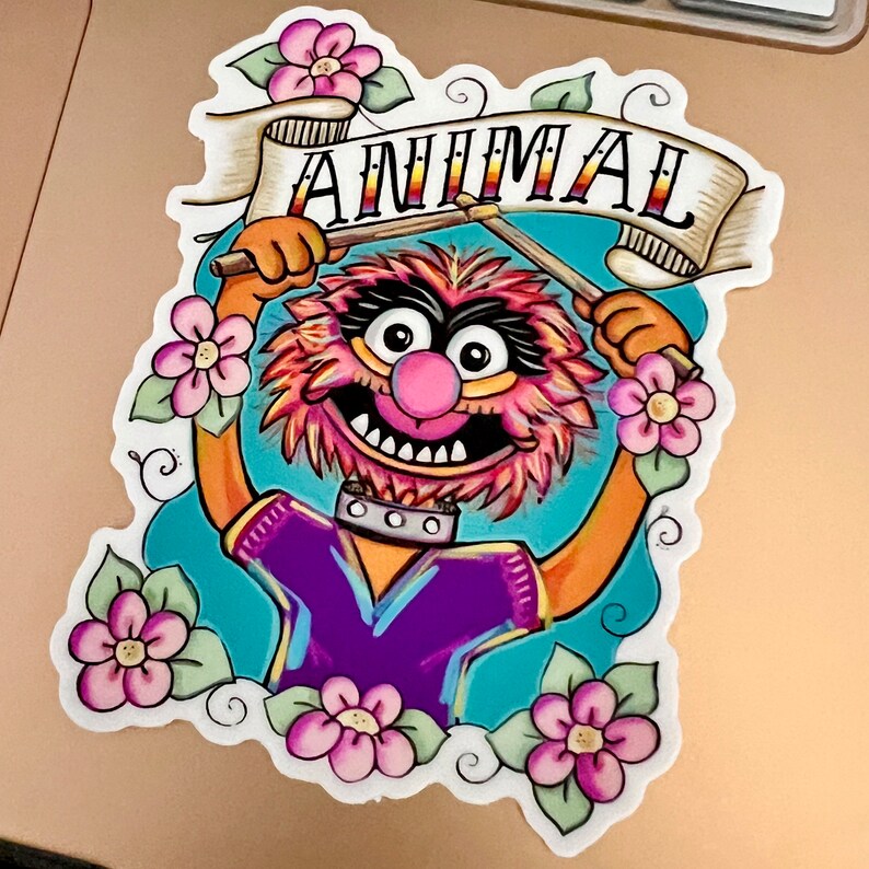 May include: A colorful illustration of Animal from the Muppets, holding drumsticks and a banner that says "ANIMAL". The illustration is surrounded by pink flowers.
