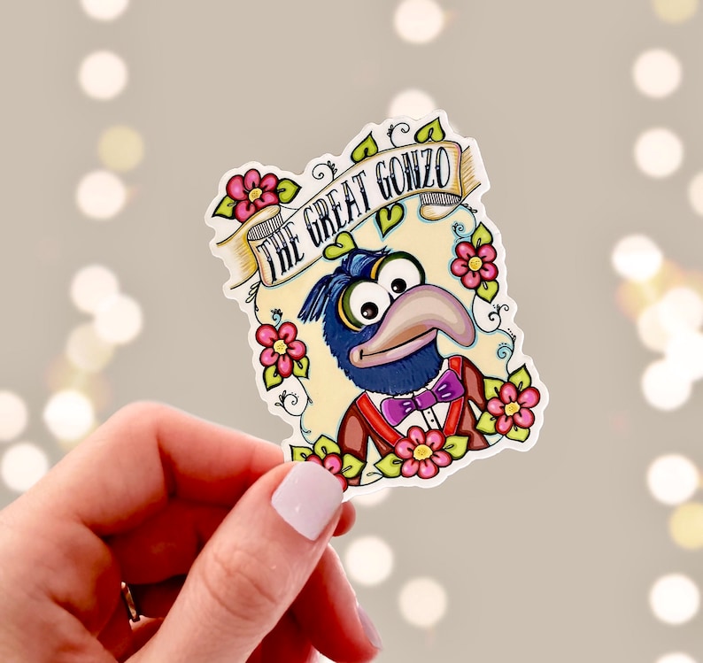 May include: A sticker featuring a cartoon illustration of Gonzo the Great from The Muppets. Gonzo is wearing a blue suit with a bow tie and is surrounded by flowers. The text "The Great Gonzo" is written in a banner above him.