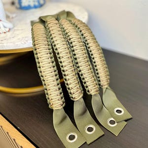 May include: Four green and tan paracord handles with metal eyelets. The handles are braided and have a textured look.