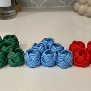 May include: A set of ten knotted fabric rings in five different colors: green, blue, red, orange, and brown. The rings are arranged in a row on a white surface.