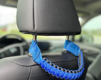 May include: A blue and black paracord car seat handle. The handle is attached to the headrest of a car seat.