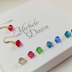 May include: A set of six crystal beads in various colours, including red, green, blue, and clear. The beads are displayed on a white box with the text "Michele Dawn" written in cursive.