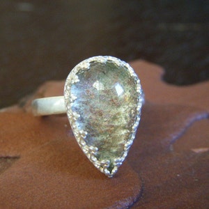 May include: A silver ring with a teardrop-shaped green and brown stone set in a silver bezel.