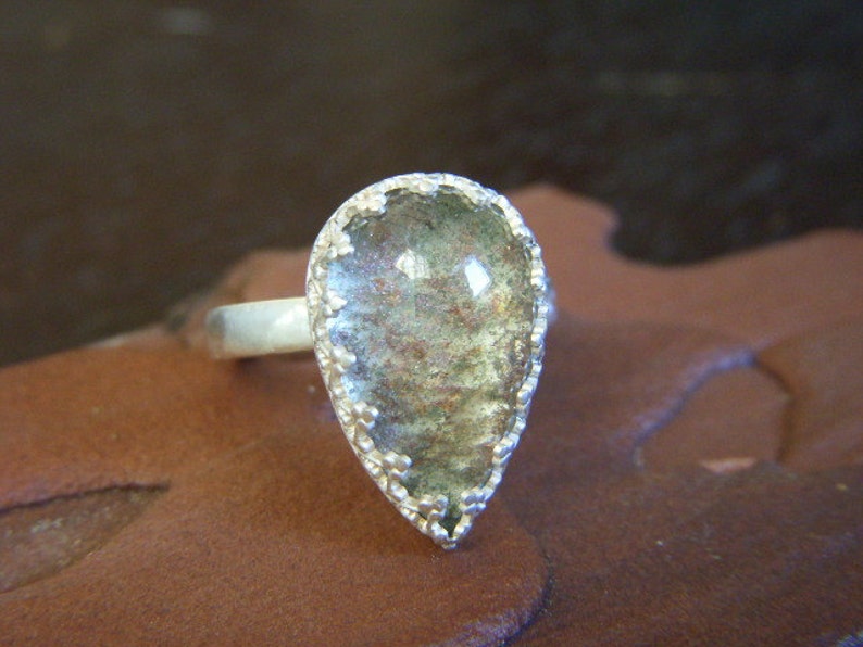May include: A silver ring with a teardrop-shaped green and brown stone set in a silver bezel.