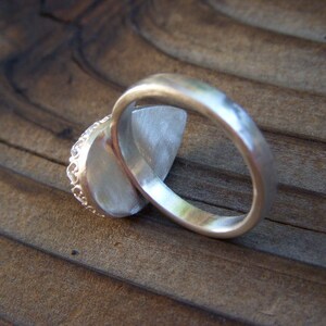 May include: A silver ring with a textured band and a large, oval-shaped gemstone. The ring is set on a wooden surface.
