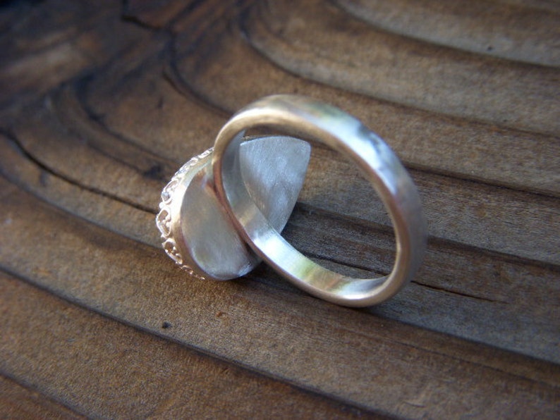 May include: A silver ring with a textured band and a large, oval-shaped gemstone. The ring is set on a wooden surface.