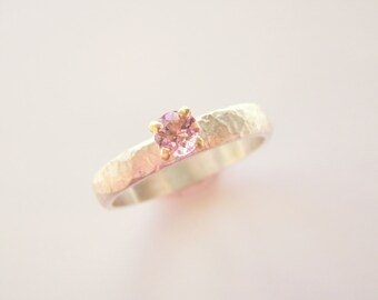 May include: A silver ring with a textured band and a small pink gemstone set in gold.