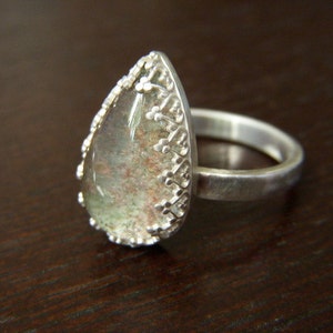 May include: A silver ring with a teardrop-shaped clear stone set in a detailed silver setting.