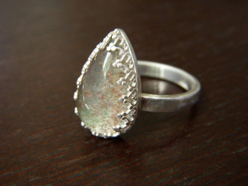 May include: A silver ring with a teardrop-shaped clear stone set in a detailed silver setting.
