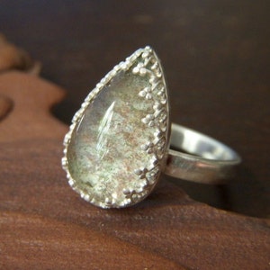 May include: A silver ring with a teardrop-shaped green gemstone set in a delicate silver filigree design.