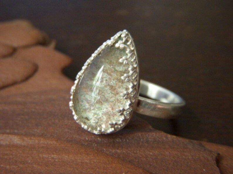 May include: A silver ring with a teardrop-shaped green gemstone set in a delicate silver filigree design.