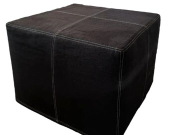 May include: A black, cube-shaped ottoman with white stitching detail. The ottoman is made from a textured material and features white stitching that forms a grid pattern on the top surface. The dimensions are approximately 60cm x 60cm x 60cm.