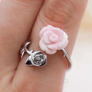 May include: A silver ring with two pink roses. The ring is adjustable and has a delicate design.