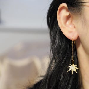 May include: Gold dangle earrings with a delicate chain and a maple leaf charm.