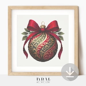 Op de afbeelding: Een ingelijste print van een kerstbal. De bal is een gedetailleerd kruissteekontwerp in rood, groen en goud, met een rode strik en groene bladeren. Het frame is van licht hout.