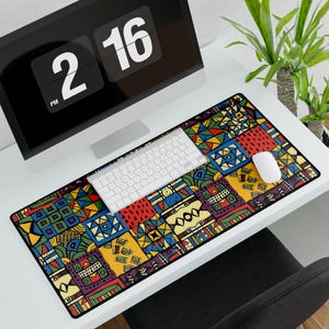 Könnte beinhalten: Eine rechteckige Schreibtischunterlage mit einem lebendigen, mehrfarbigen geometrischen Patchwork-Muster aus roten, gelben, blauen und grünen Quadraten. Die Unterlage liegt auf einem weißen Schreibtisch unter einer weißen Tastatur und Maus.