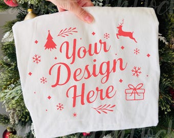 Könnte beinhalten: Ein weißes Kissenbezug mit dem roten Text "Your Design Here". Das Design umfasst einen Weihnachtsbaum, Schneeflocken, ein Rentier und eine Geschenkbox. Der Kissenbezug wird vor einem Weihnachtsbaum gehalten.
