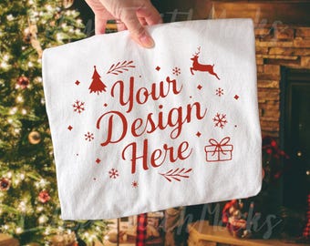 Könnte beinhalten: Weißes rechteckiges Handtuch mit roten weihnachtlichen Grafiken und dem Text "Your Design Here". Das Design umfasst einen Weihnachtsbaum, Schneeflocken, ein Rentier und eine Geschenkbox. Das Handtuch wird vor einem Weihnachtsbaum und einem Kamin gehalten.