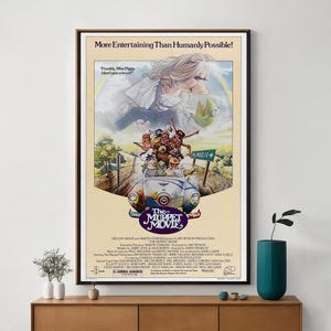 May include: A framed poster for "The Muppet Movie." The artwork features Miss Piggy, Kermit, and other Muppet characters in a colourful, whimsical design. The text at the top reads "More Entertaining Than Humanly Possible!" and the movie title is displayed.