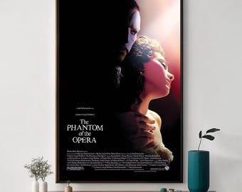 May include: Framed poster for "The Phantom of the Opera" musical. The image features a man in a mask and a woman in profile, with the title in white text. The poster is in a black frame.