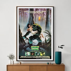 Puede incluir: Un póster de película vintage para la película Swamp Thing. El póster presenta un monstruo de pantano verde sosteniendo a una mujer en sus brazos. El texto en el póster dice "La ciencia lo transformó en un monstruo. ¡El amor lo cambió aún más!" y "Swamp Thing: ¡La leyenda del cómic vive!"