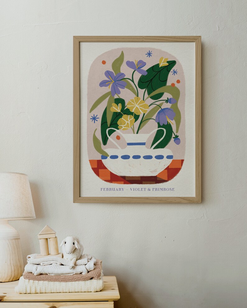 May include: A framed illustration of a white ceramic vase with a blue rim filled with purple violets and yellow primroses. The vase is sitting on a red and orange checkered surface. The text "FEBRUARY - VIOLET & PRIMROSE" is at the bottom of the illustration.