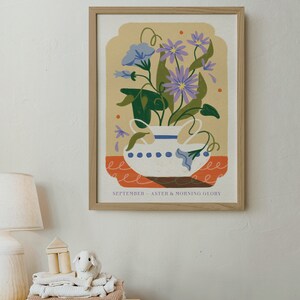 Op de afbeelding: Een ingelijste illustratie van een witte vaas met blauwe en witte stippen gevuld met paarse en blauwe bloemen. De tekst "SEPTEMBER - ASTER & MORNING GLORY" staat onderaan de illustratie.