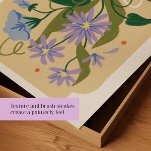 Op de afbeelding: Een ingelijste print van een bloemenillustratie met paarse bloemen, groene bladeren en oranje stippen op een beige achtergrond. De tekst "Texture and brush strokes create a painterly feel" is zichtbaar onderaan de print.
