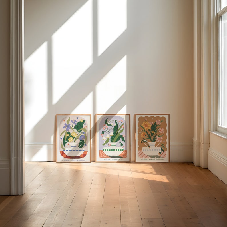 May include: Three framed prints with floral illustrations in a white room with wooden floors. The prints feature different floral arrangements in vases with text below each image. The text reads "Sometimes I Wish I Was A Mermaid", "What I Love In The Valley", and "In Order, Wandering & Wonder".
