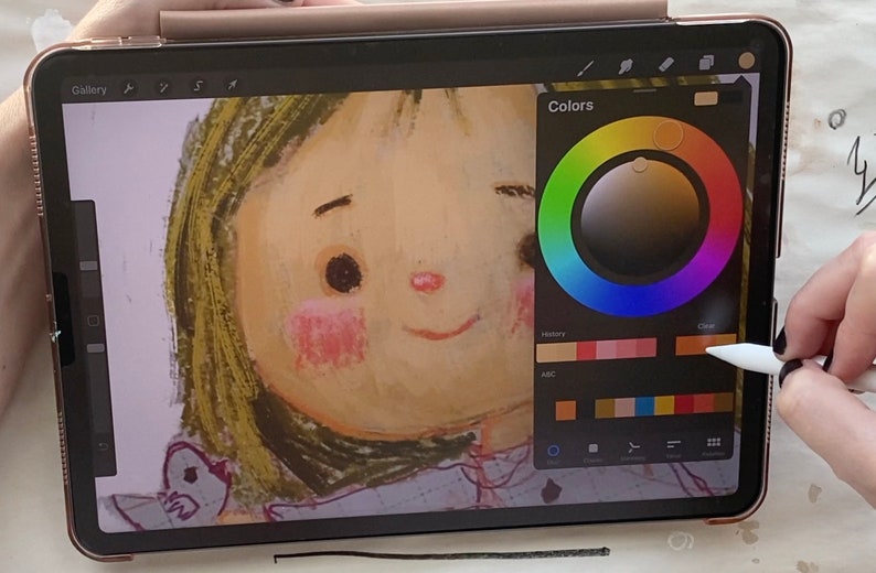 May include: A digital illustration of a girl's face on a tablet screen. The tablet is being used with a stylus to select colors from a color wheel on the screen. The color wheel has a variety of colors, including red, orange, yellow, green, blue, indigo, and violet. The girl's face is drawn in a cartoon style with large eyes and a wide smile.