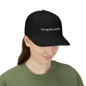 May include: A black baseball cap featuring a mesh back and a solid front panel. The text "incognito mode." is embroidered in white, lowercase, serif font across the centre of the front panel. The cap has a structured crown and a flat brim.