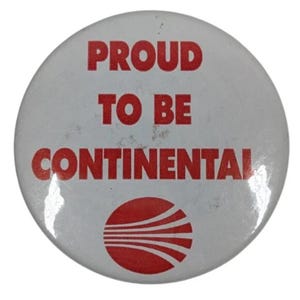 May include: A round, white button with the text "PROUD TO BE CONTINENTAL" in red, bold letters. Below the text is a red graphic of a stylized airplane. The button has a slightly worn appearance.