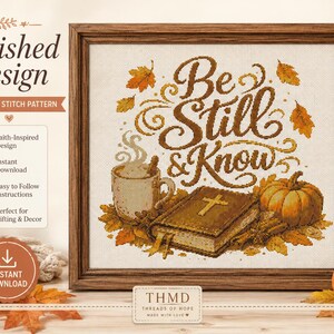 Op de afbeelding: Een ingelijst kruissteekpatroon met de tekst Be Still & Know in bruin handschrift. Het kunstwerk bevat een dampende mok, een gesloten boek met een gouden kruis op de kaft en oranje herfstbladeren rondom de centrale belettering.