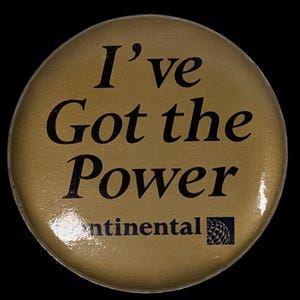 May include: A round, gold-colored button with the phrase "I've Got the Power" in black lettering. The word "continental" is printed below the phrase, along with a black and white logo.