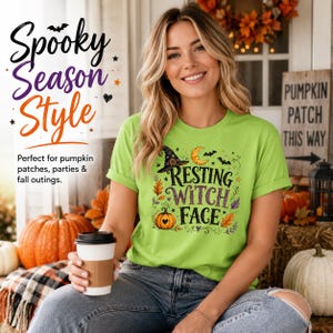 Op de afbeelding: Een limoengroen t-shirt met een grafische print met de tekst "RESTING WITCH FACE" in zwarte en paarse letters, vergezeld van illustraties van een heksenhoed, een maansikkel, vleermuizen, herfstbladeren en een kleine oranje pompoen.