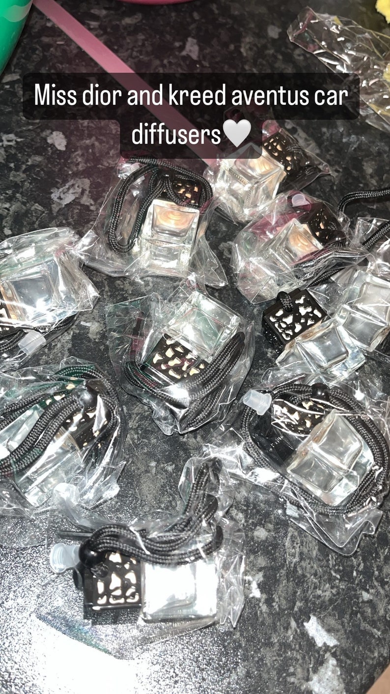 May include: Multiple clear glass car diffusers with black metal accents and black string hangers. The diffusers are packaged in clear plastic bags. The text "Miss dior and kreed aventus car diffusers" is visible in the image.