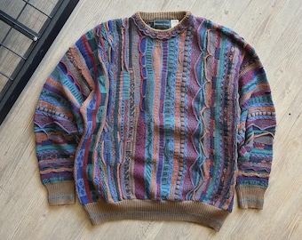 Op de afbeelding: Een vintage, veelkleurige trui met een textuur gebreid ontwerp. De trui heeft een mix van verticale en patroonstrepen in tinten blauw, paars, groen en bruin. Het heeft een ronde hals en geribde manchetten en zoom. De trui is gemaakt van een zacht materiaal.