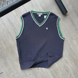 May include: Navy blue V-neck sweater vest with green and white trim. The vest has a small embroidered leaf design and the word "BOAST" on the label. The vest is made of a textured knit fabric.