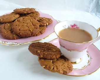 Op de afbeelding: Een roze theekopje en schotel met een bloemenpatroon, gevuld met thee, en een bord met pindakaas koekjes.