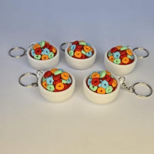 May include: Five keychains featuring miniature white bowls filled with colorful cereal. Each bowl contains red, orange, blue, and green cereal pieces. The keychains have silver-colored rings.