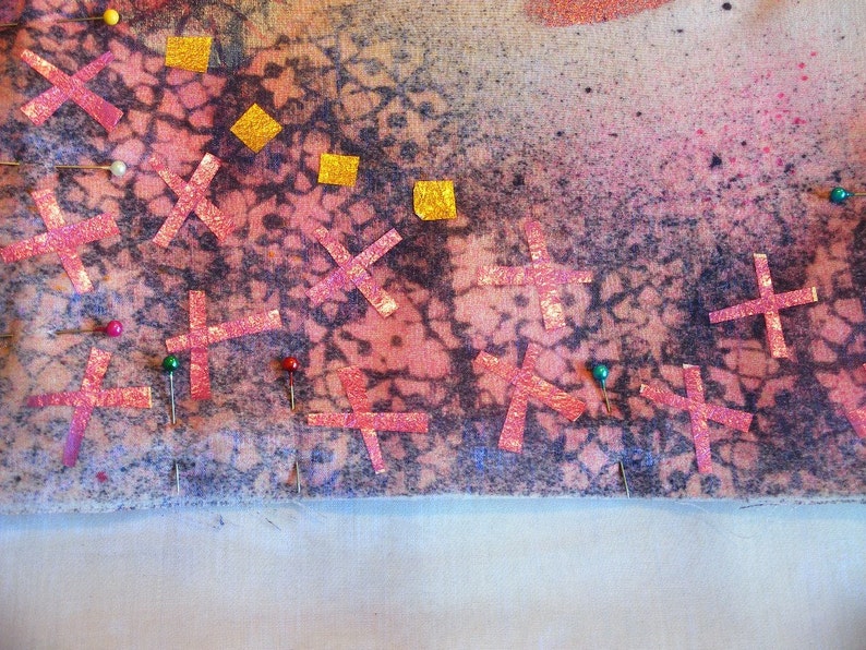 Pu&ograve; includere: Primo piano di un tessuto con un motivo rosa e viola. Il tessuto &egrave; fissato con spilli rossi e verdi. Ci sono anche quadrati dorati e croci rosa sul tessuto.