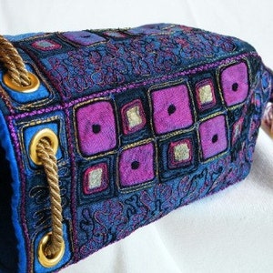 May include: A blue and purple fabric bag with a drawstring closure and a tassel. The bag is decorated with embroidered geometric shapes and floral patterns.