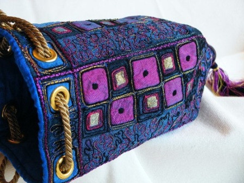 May include: A blue and purple fabric bag with a drawstring closure and a tassel. The bag is decorated with embroidered geometric shapes and floral patterns.