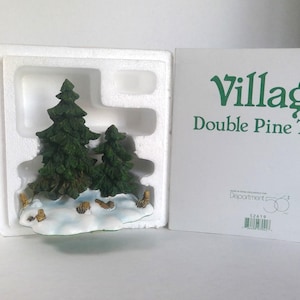 May include: A miniature village scene featuring two green pine trees on a snowy base. The trees are set in a white styrofoam container, with the product's name, "Village Double Pine Trees," printed on the accompanying box.