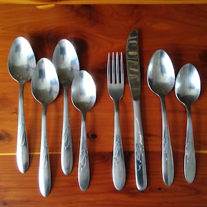 May include: A set of silverware, including a fork, knife, and six spoons. The silverware is made of stainless steel and has a polished finish.