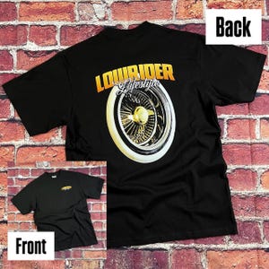 Puede incluir: Camiseta negra con un gráfico dorado y blanco de una rueda de lowrider y las palabras "Lowrider Lifestyle". La parte delantera de la camiseta tiene un pequeño logotipo dorado. La camiseta se muestra contra una pared de ladrillos.