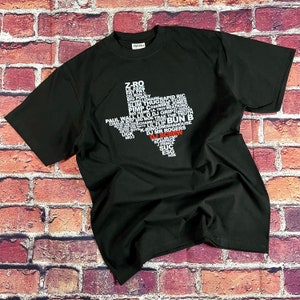 Può includere: T-shirt nera con grafica bianca dello stato del Texas piena di nomi. La parola "DJ SCREW" è in rosso. La maglietta è realizzata in un materiale morbido.