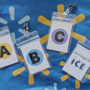 May include: Four clear plastic badge holders with metal clips. Each holder contains a white card with a letter or text. Letters A, B, and C are in yellow, blue, and purple circles. The fourth card reads "Don't forget the ICE".