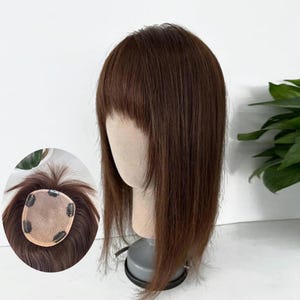 May include: A medium brown hair topper with straight strands and bangs displayed on a mannequin head. An inset circular view shows the underside of the hairpiece, featuring a beige mesh base with four small metal pressure-sensitive clips attached.