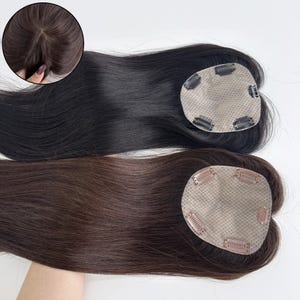 May include: Two hair toppers, one black and one brown, are displayed against a white background. Each topper has a mesh base with clips for attachment. A close-up shows the hair's natural appearance.
